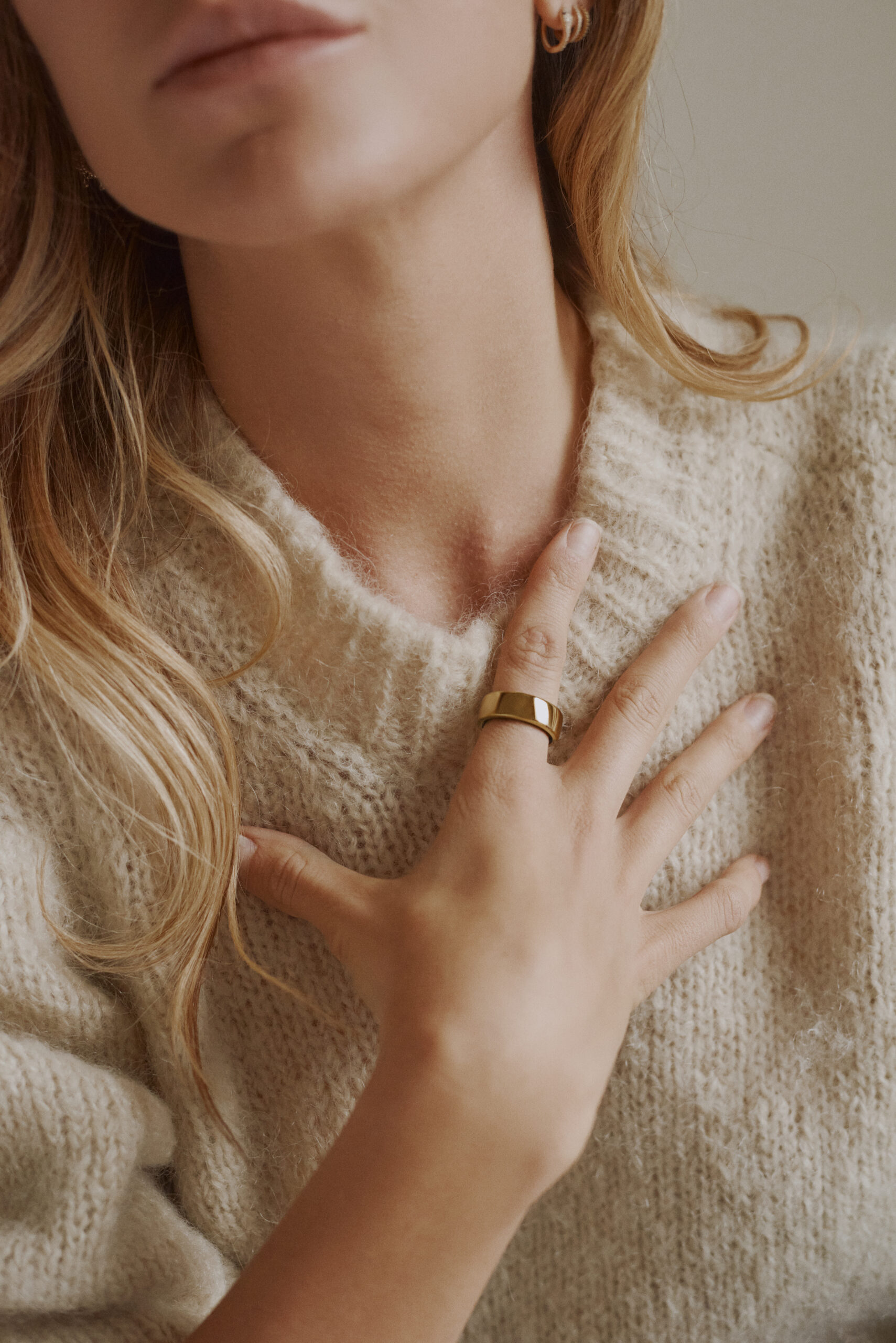 Woman wearing white sweater and gold Oura Ring